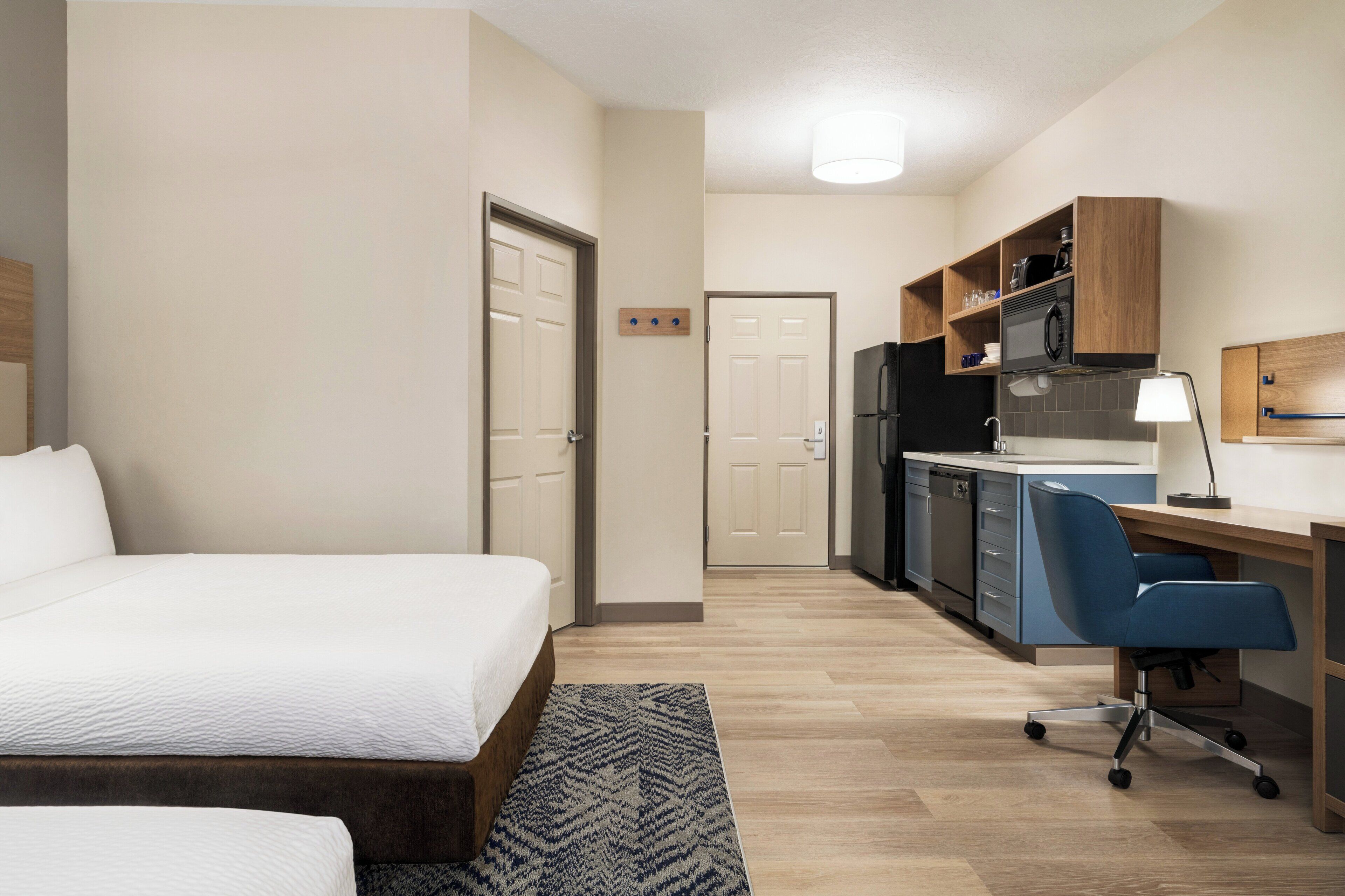 Una habitación de hotel con cama, escritorio, silla, refrigerador y microondas.