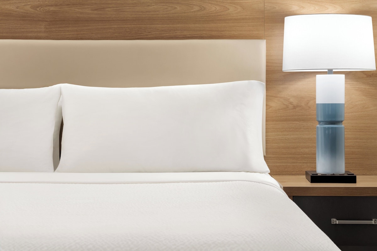 Un letto rifatto con lenzuola bianche e un moderno comodino con una lampada.