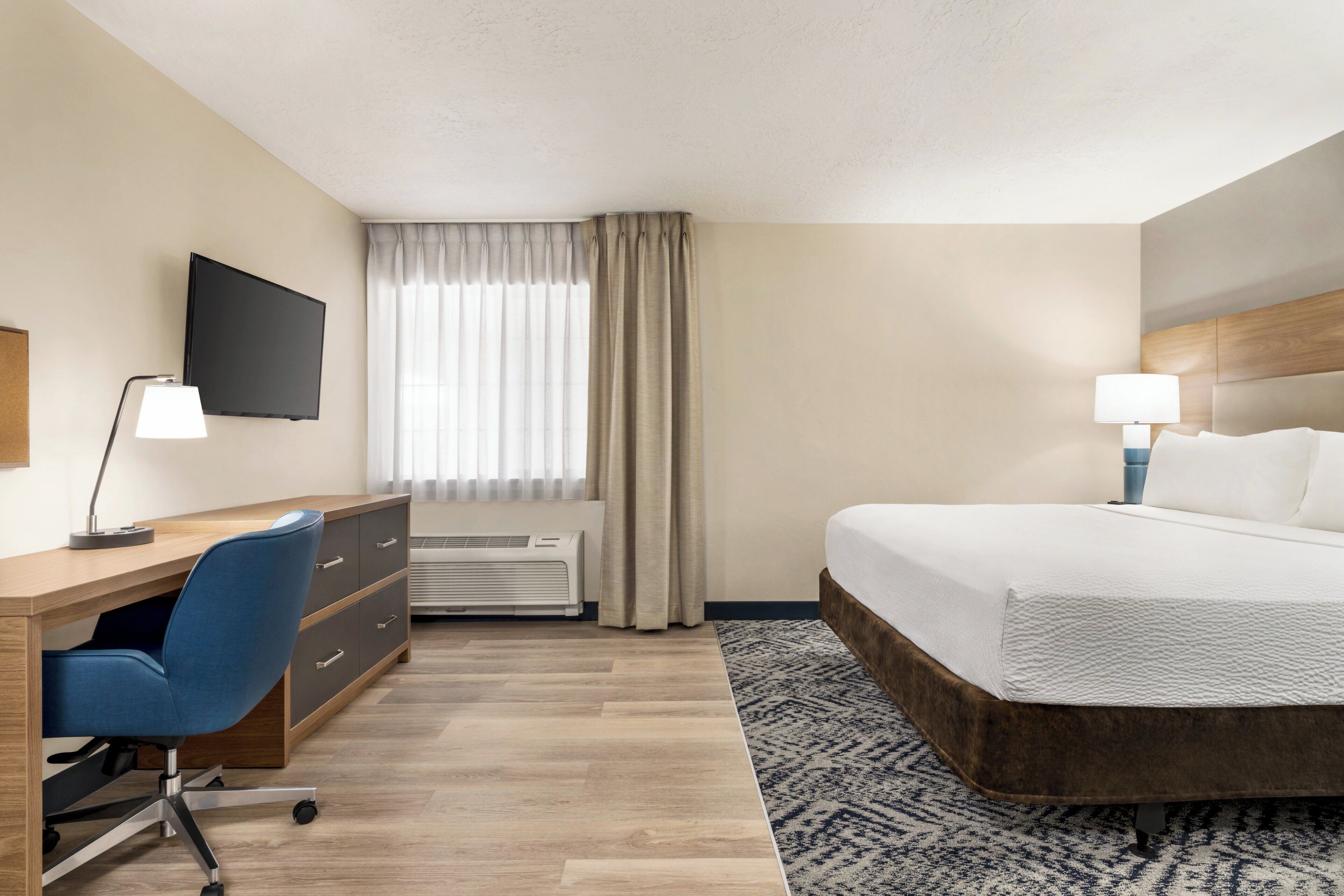 Une chambre d’hôtel équipée d’un lit, d’un bureau, d’une chaise, d’une télévision et d’une fenêtre avec des rideaux.