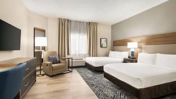 A hotel room with a desk, two beds, a chair, a TV, and a window with curtains.