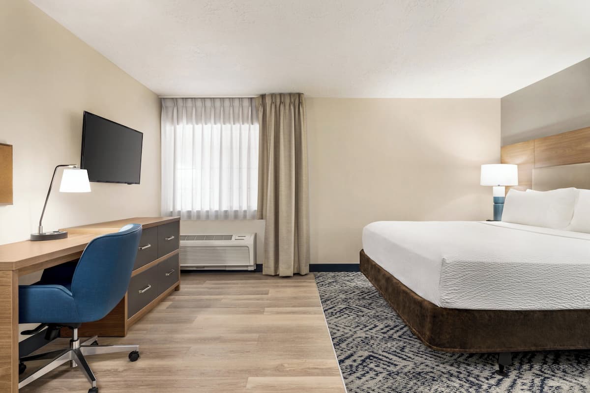 Een hotelkamer met een bed, bureau, stoel, televisie en een raam met gordijnen.