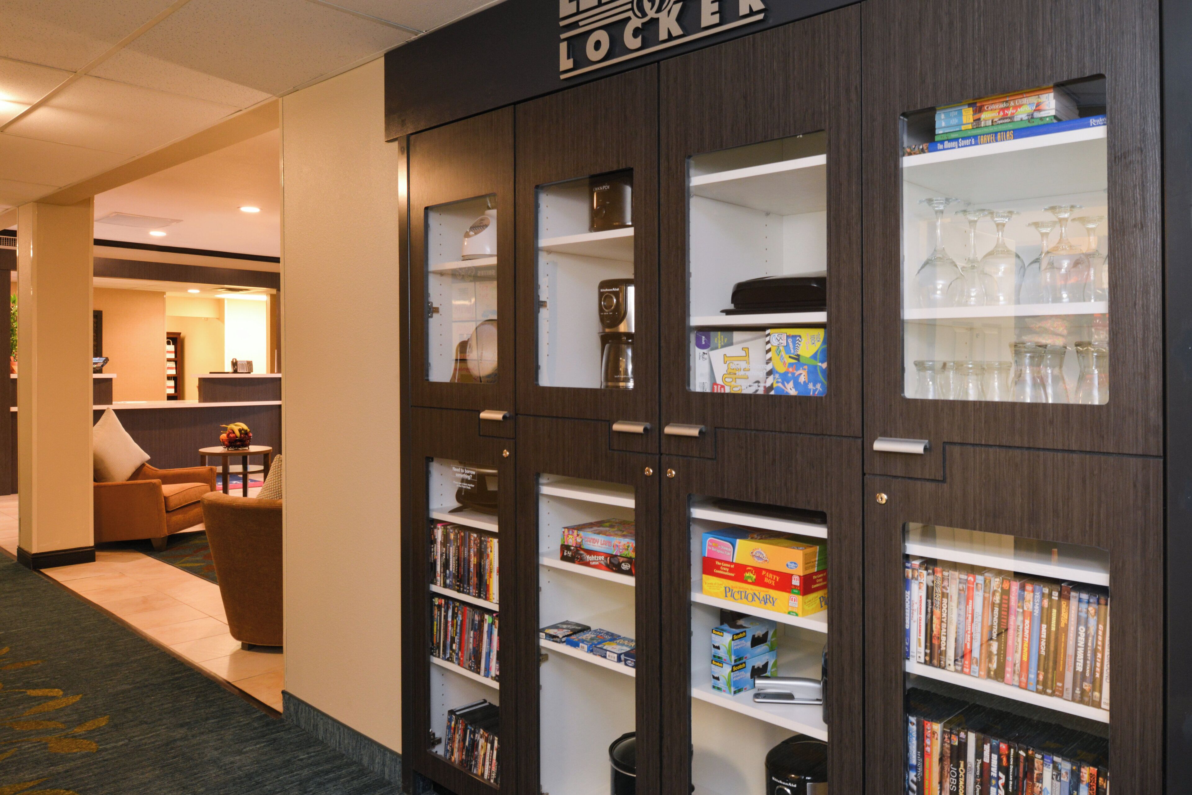 A hotel lobby with a reception desk, seating area, and a bookshelf filled with books and board games.