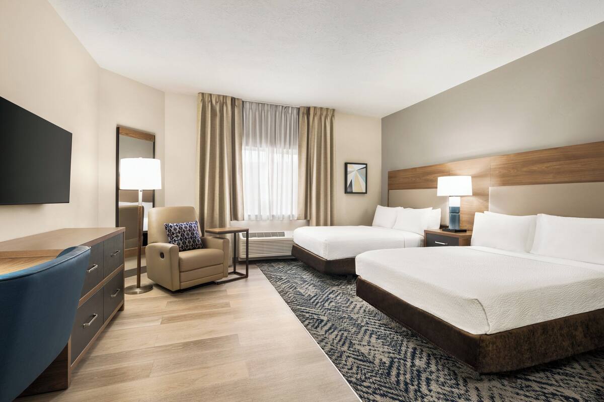 Hotelkamer met een bureau, twee bedden, een stoel, een televisie en een raam met gordijnen.