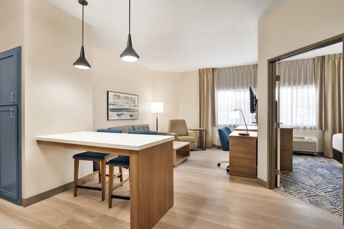 Een hotelkamer met kitchenette, eethoek, bank, bureau en bed.