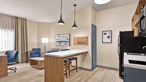 A modern hotel room with a kitchenette, a dining area with a bar, a seating area with a sofa and chairs, and a large window with curtains. - Candlewood Suites Boise - Towne Square by IHG (Boise)