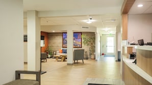 A modern reception area with a wooden reception desk, a seating area with a sofa and chairs, and a large window with a cityscape view. - Candlewood Suites Boise - Towne Square by IHG (Boise)