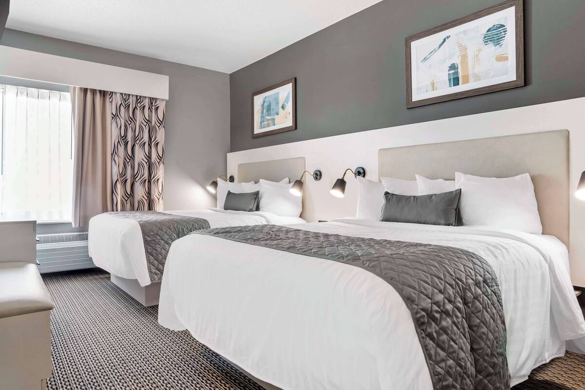 Une chambre d’hôtel avec deux lits, une grande fenêtre avec des rideaux et des œuvres d’art accrochées aux murs.