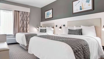 Een hotelkamer met twee bedden, een groot raam met gordijnen, en kunstwerken aan de muur.