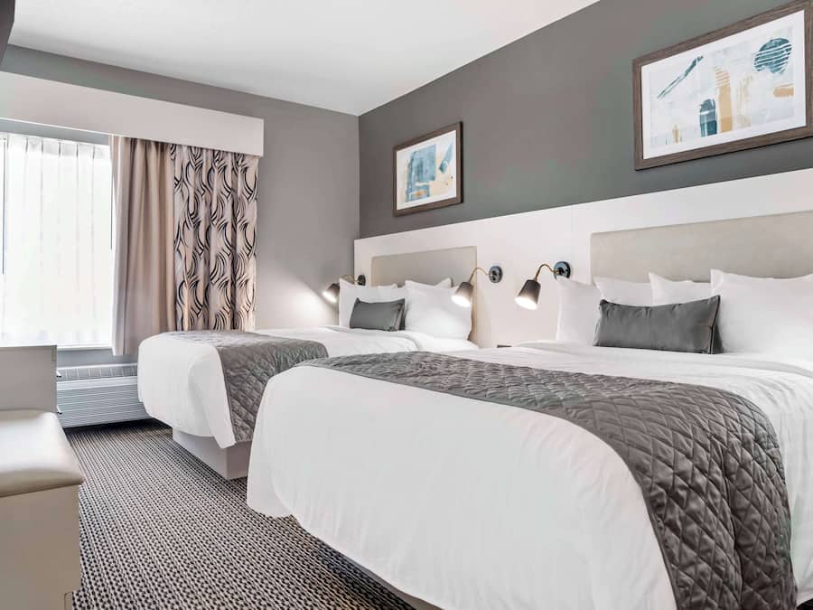 Een hotelkamer met twee bedden, een groot raam met gordijnen, en kunstwerken aan de muur.