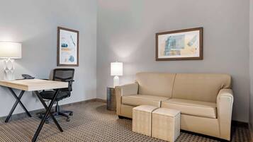 A room with a desk, office chair, beige sofa, and two ottomans. There are two framed artworks on the walls.