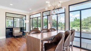 A spacious dining area with a large wooden table and leather chairs, large windows with a view of greenery, and a modern chandelier. - Best Western Plus Two Rivers Hotel & Suites (Demopolis)