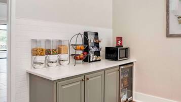 A kitchen with a white countertop, a coffee machine, a microwave, and a refrigerator.