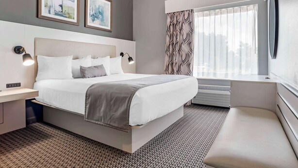 A modern hotel room with a large bed, bedside tables, a bench, and a window with curtains. - Best Western Plus Two Rivers Hotel & Suites (Demopolis)
