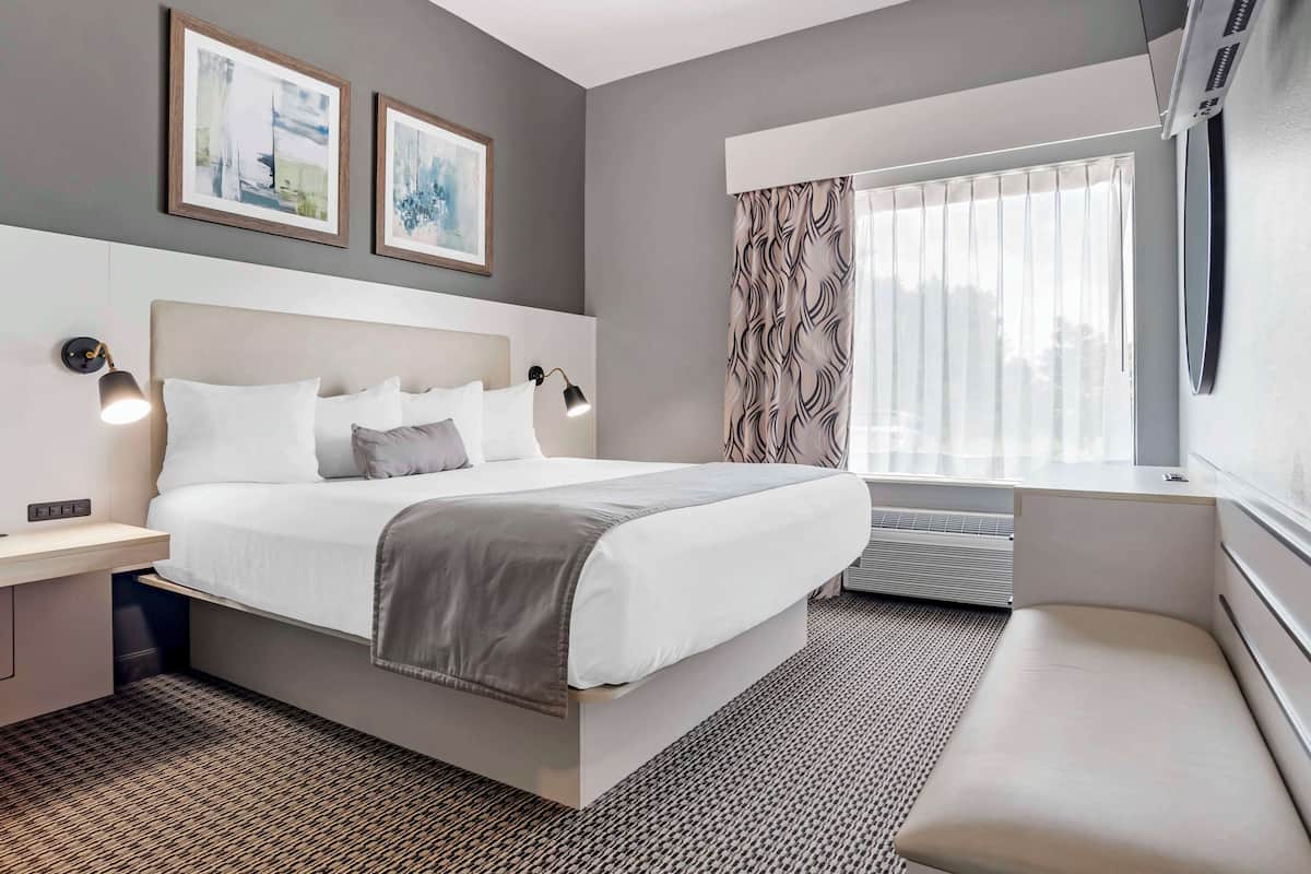 Une chambre d’hôtel moderne avec un grand lit, des tables de chevet, un banc et une fenêtre avec des rideaux.