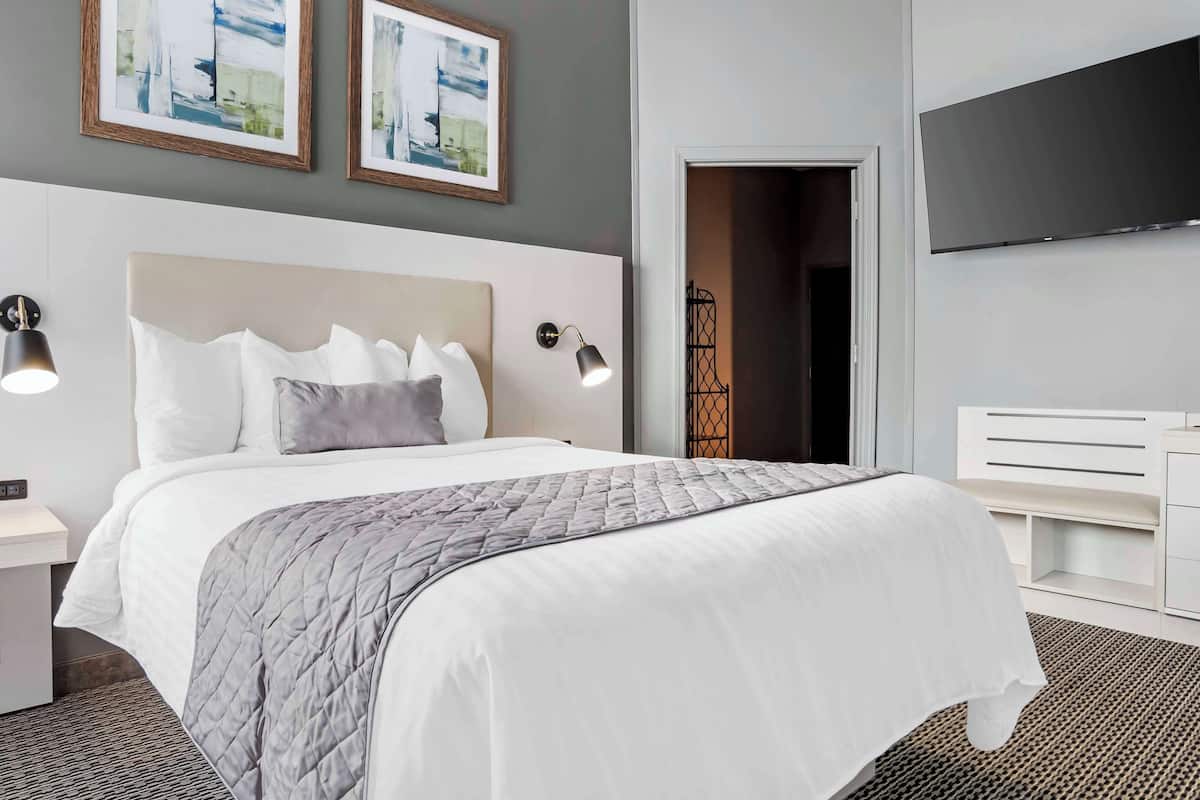 Une chambre d’hôtel bien aménagée, avec un grand lit, des lampes de chevet, un téléviseur à écran plat et des œuvres d’art accrochées au mur.