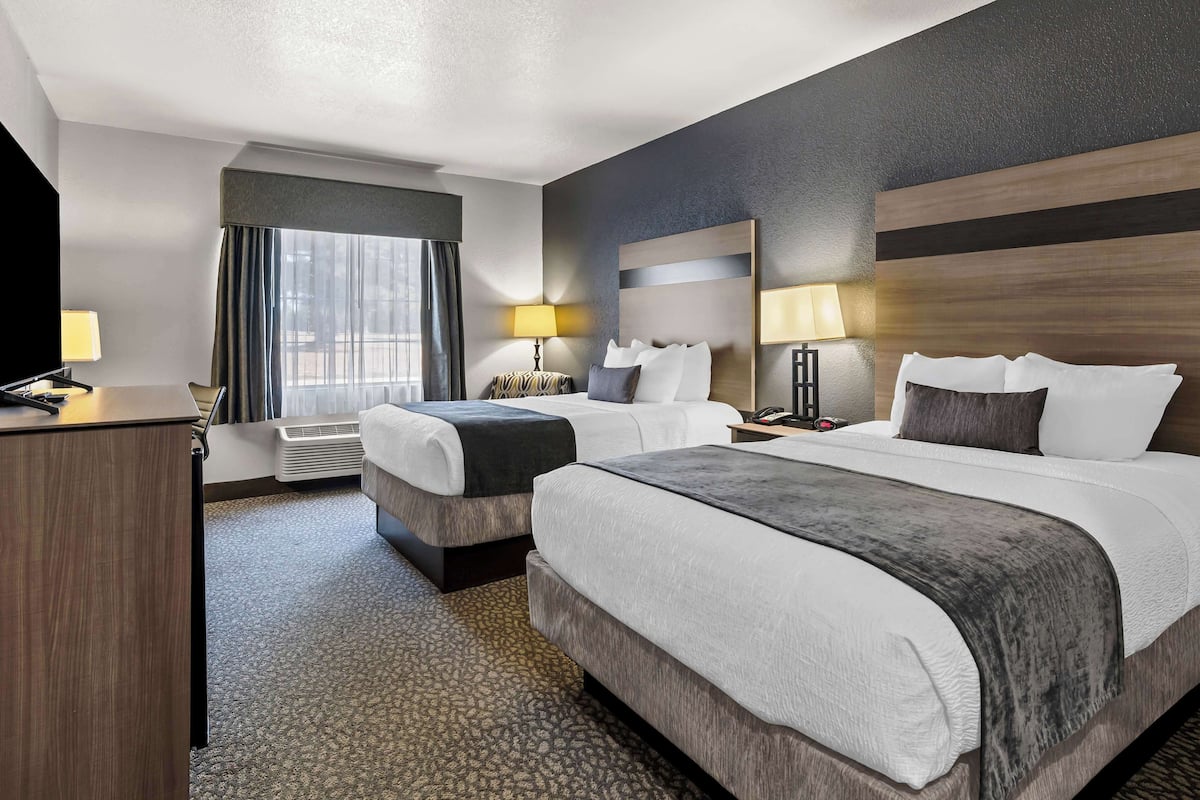Une chambre d’hôtel avec deux lits, un bureau, une chaise, une télévision et une fenêtre avec des rideaux.