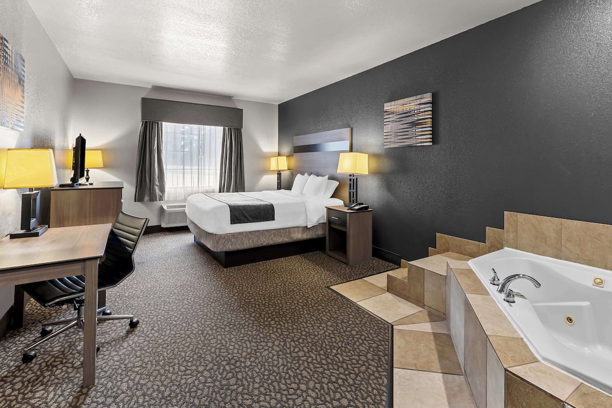 Une chambre d’hôtel équipée d’un lit, d’un bureau, d’une chaise, de lampes et d’une baignoire.