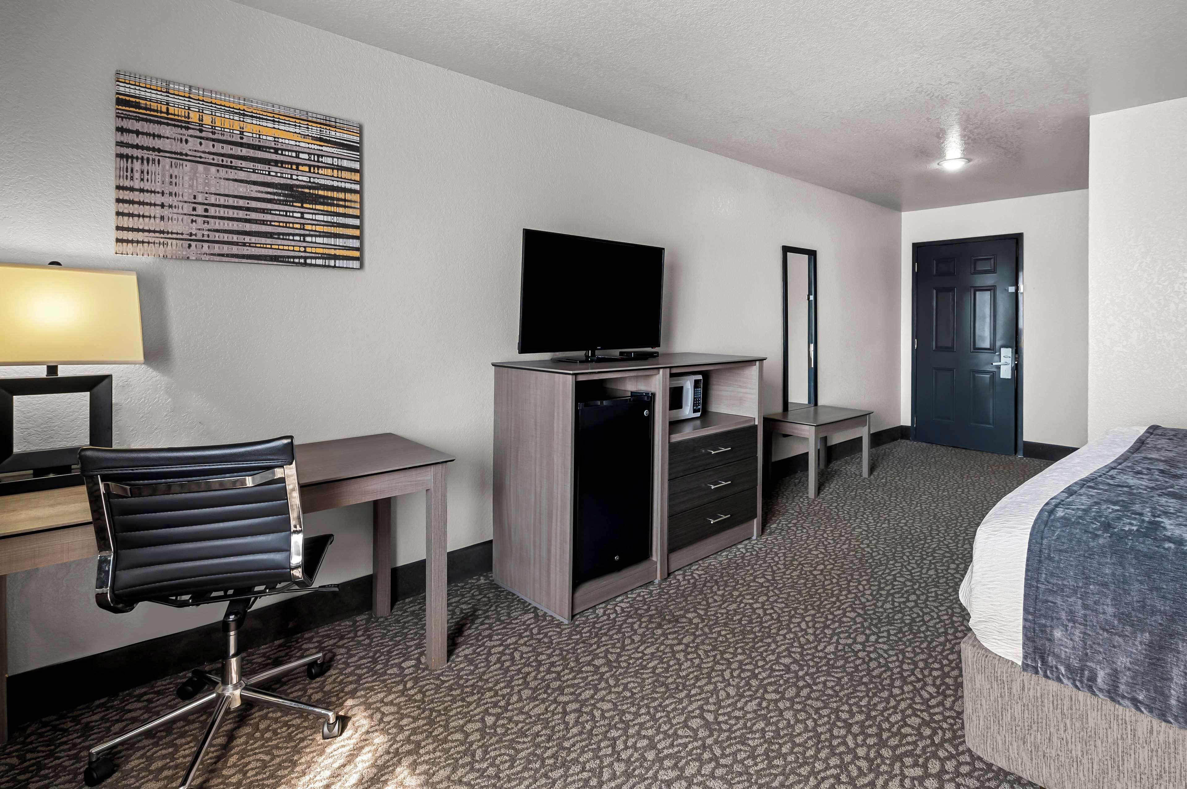 Habitación de hotel con cama, escritorio, silla, televisión, microondas y espejo.