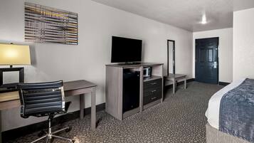Habitación de hotel con cama, escritorio, silla, televisión, microondas y espejo.