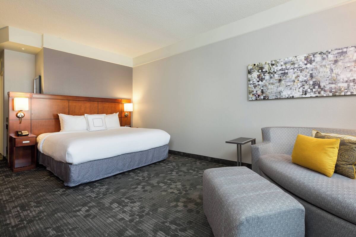 Une chambre d’hôtel avec un lit, un canapé, une petite table et une œuvre d’art accrochée au mur.