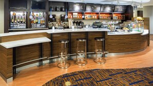 A modern bar area with a curved counter, three stools, and a variety of beverages and snacks.