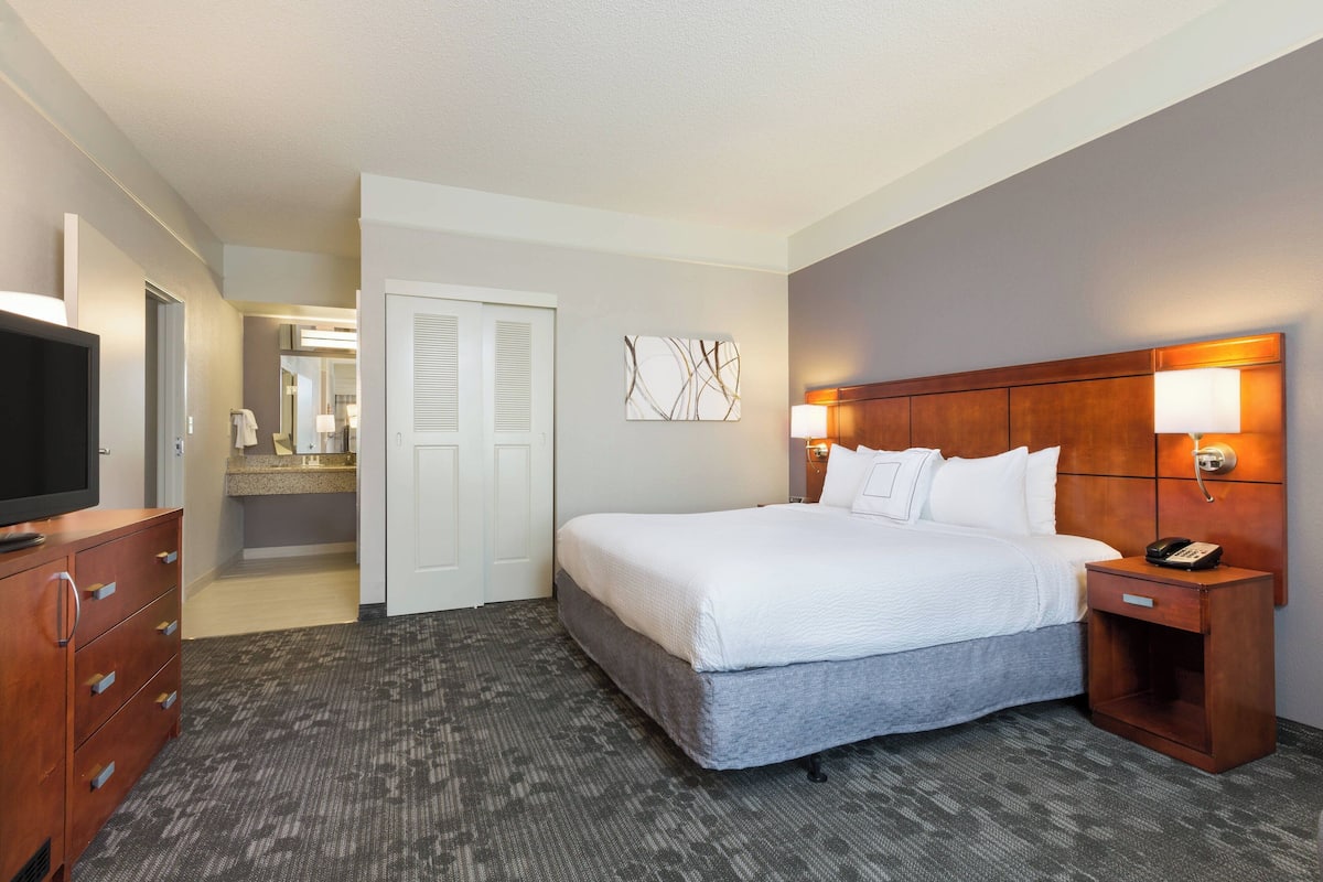 Une chambre d’hôtel avec un lit, une table de chevet, une lampe et un téléviseur posé sur une commode.