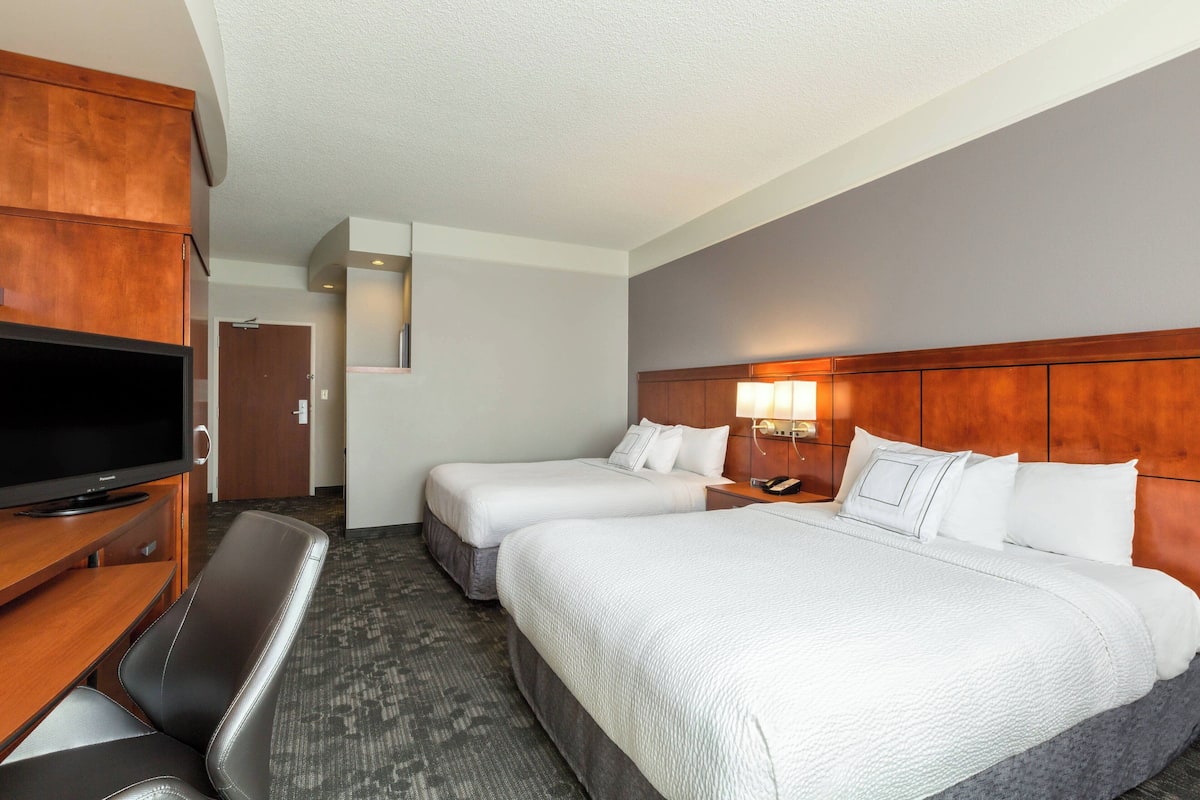 Une chambre d’hôtel avec deux lits, une télévision, un bureau et une chaise.
