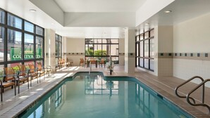 An indoor swimming pool with lounge chairs and a table, large windows, and a view of the outside.