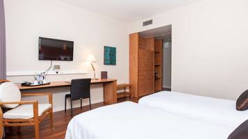 A hotel room with two beds, a desk with a chair, a TV mounted on the wall, and a wooden wardrobe.