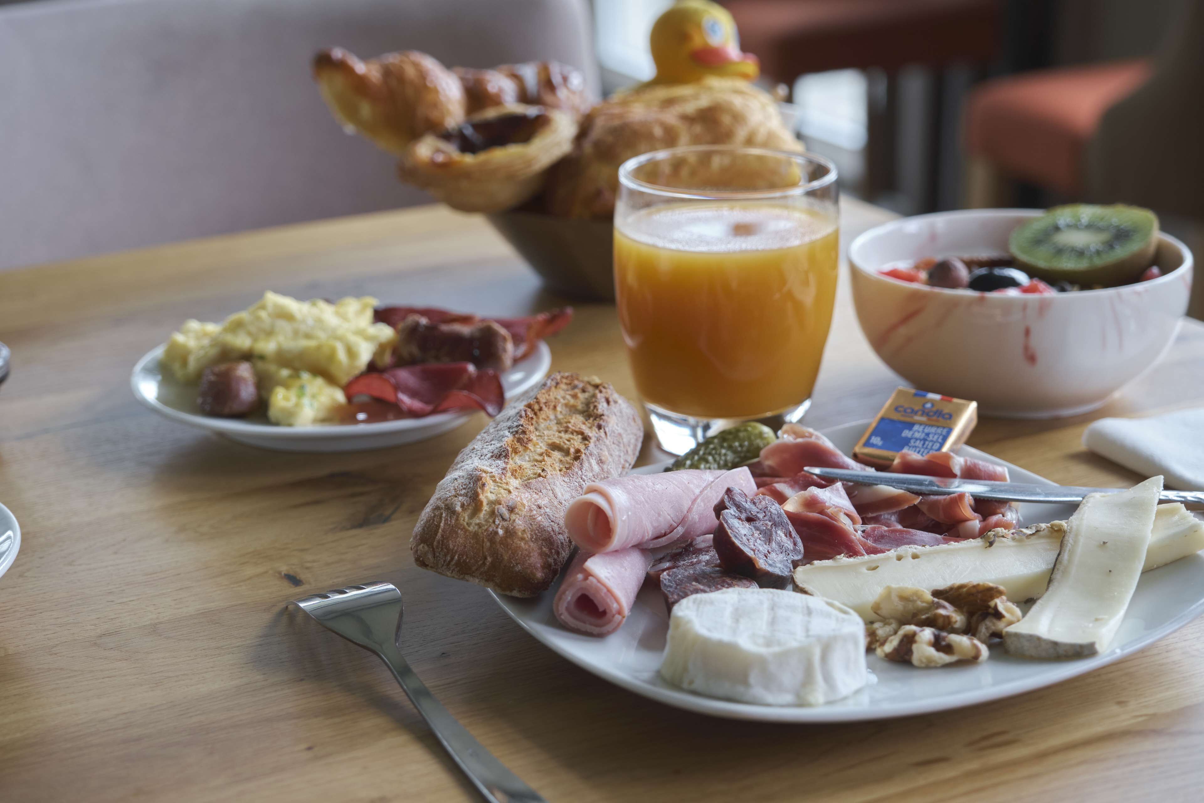 Un plato de desayuno con diversos alimentos, incluyendo huevos, jamón, queso y un vaso de jugo de naranja.