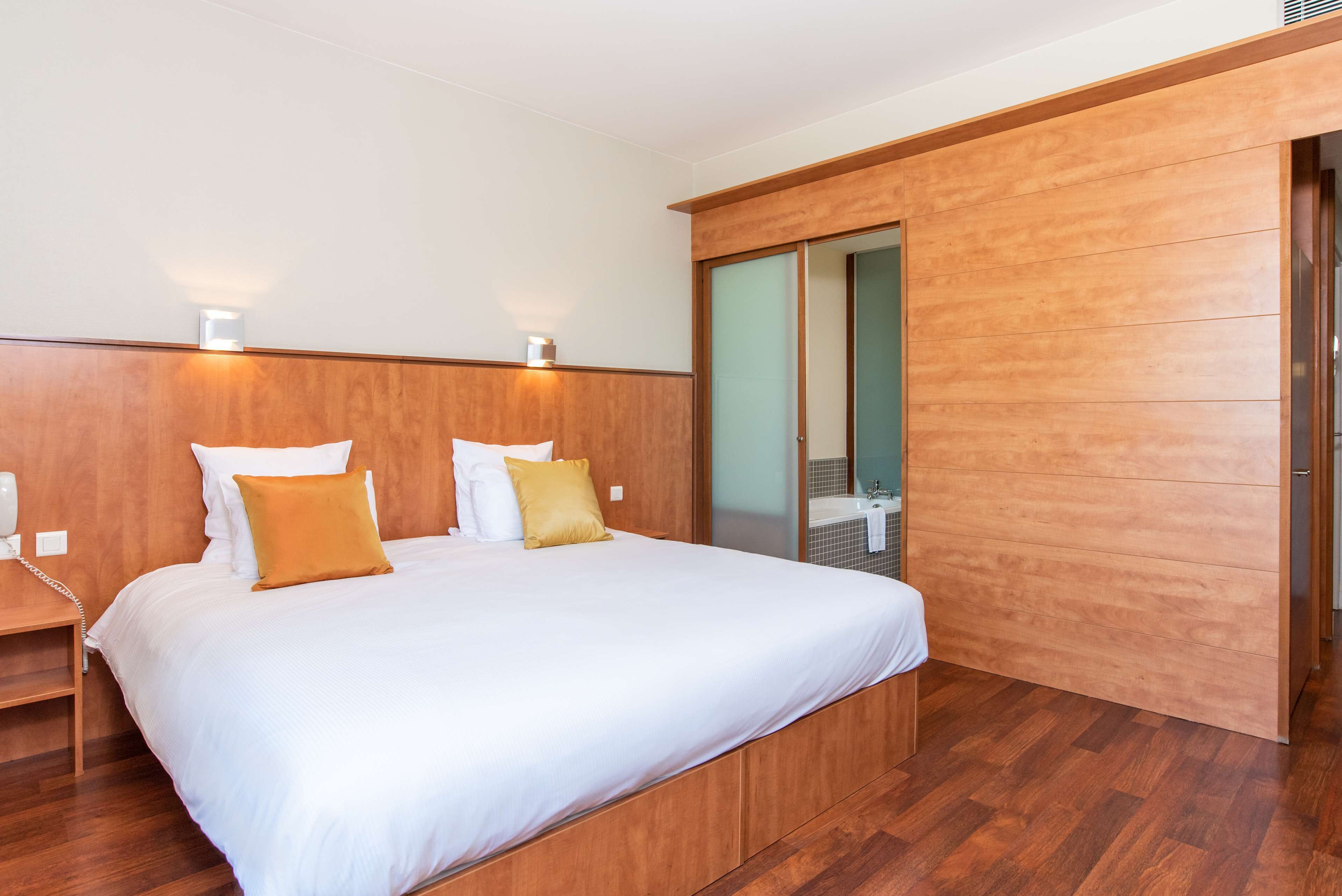A hotel room with a large bed, wooden headboard, and a sliding door leading to a bathroom.