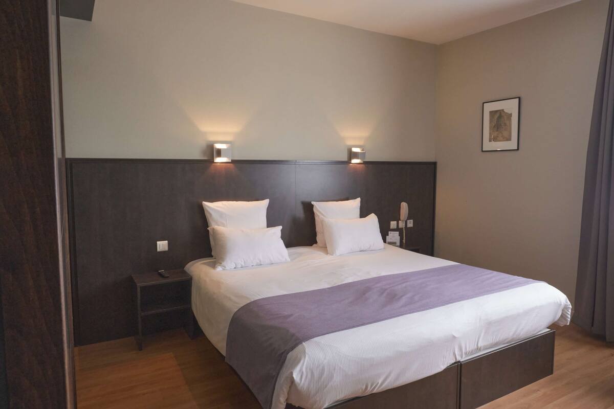 A modern hotel room with a large bed, two bedside lamps, a nightstand, and a framed picture on the wall.