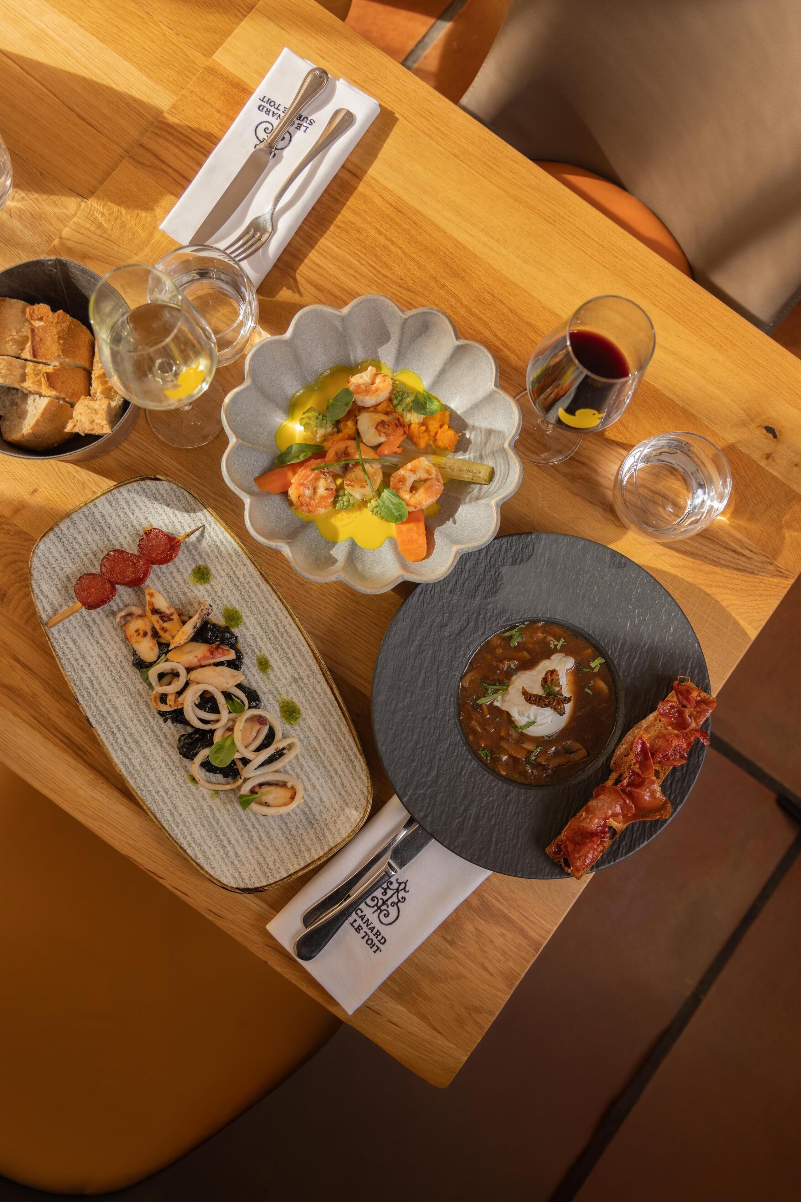 A wooden table with various dishes, including seafood, vegetables, and bread.