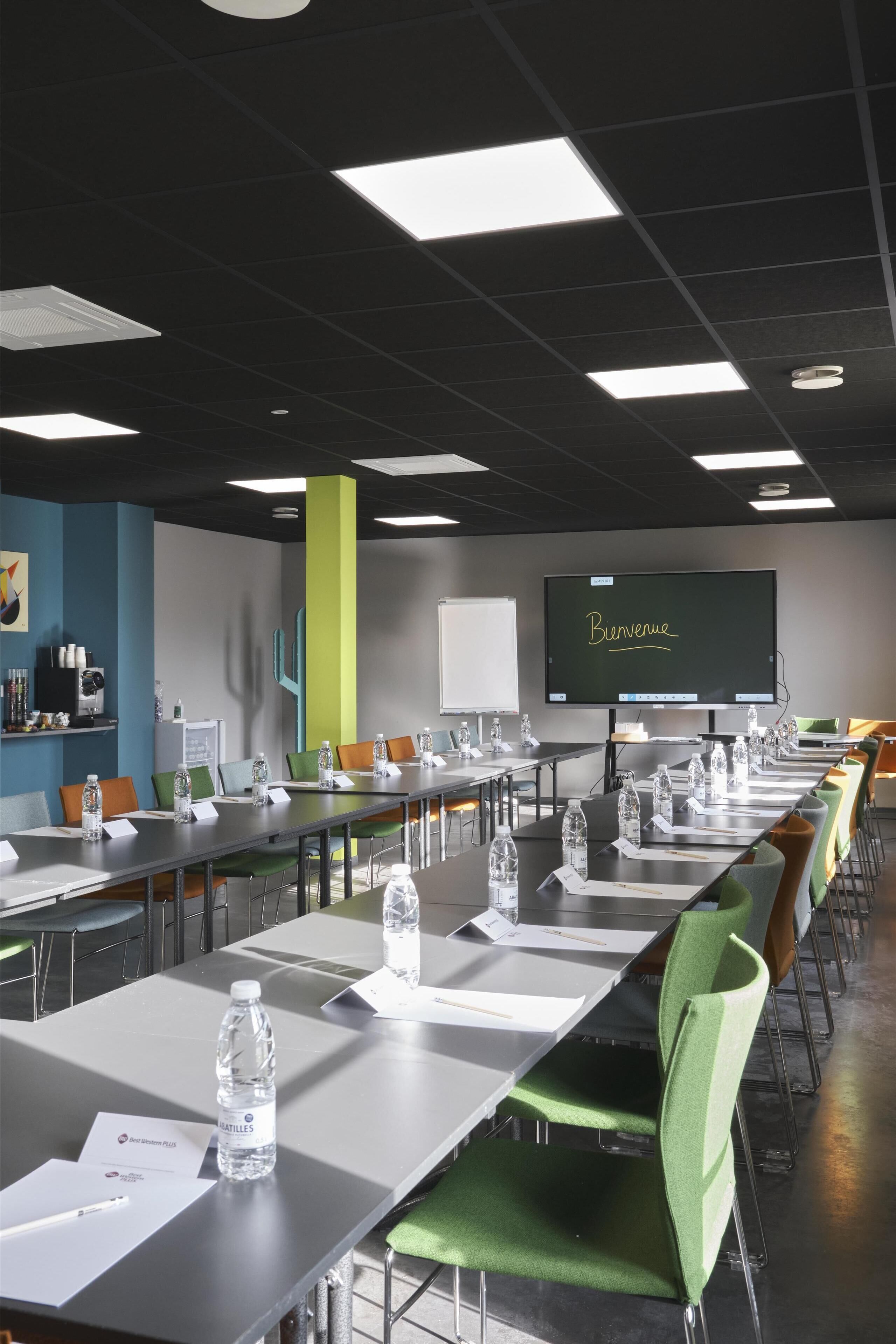 A conference room with tables, chairs, water bottles, and a projector screen displaying "Bienvenue".