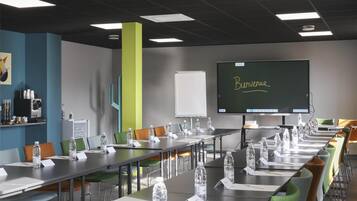 A conference room with tables, chairs, water bottles, and a projector screen displaying "Bienvenue".