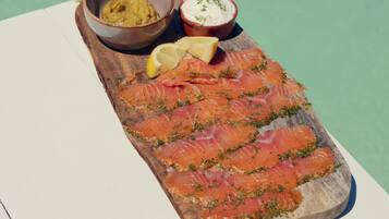 Una tabla de madera con salmón ahumado, un recipiente de mostaza y un tazón pequeño de queso crema decorado con hierbas.