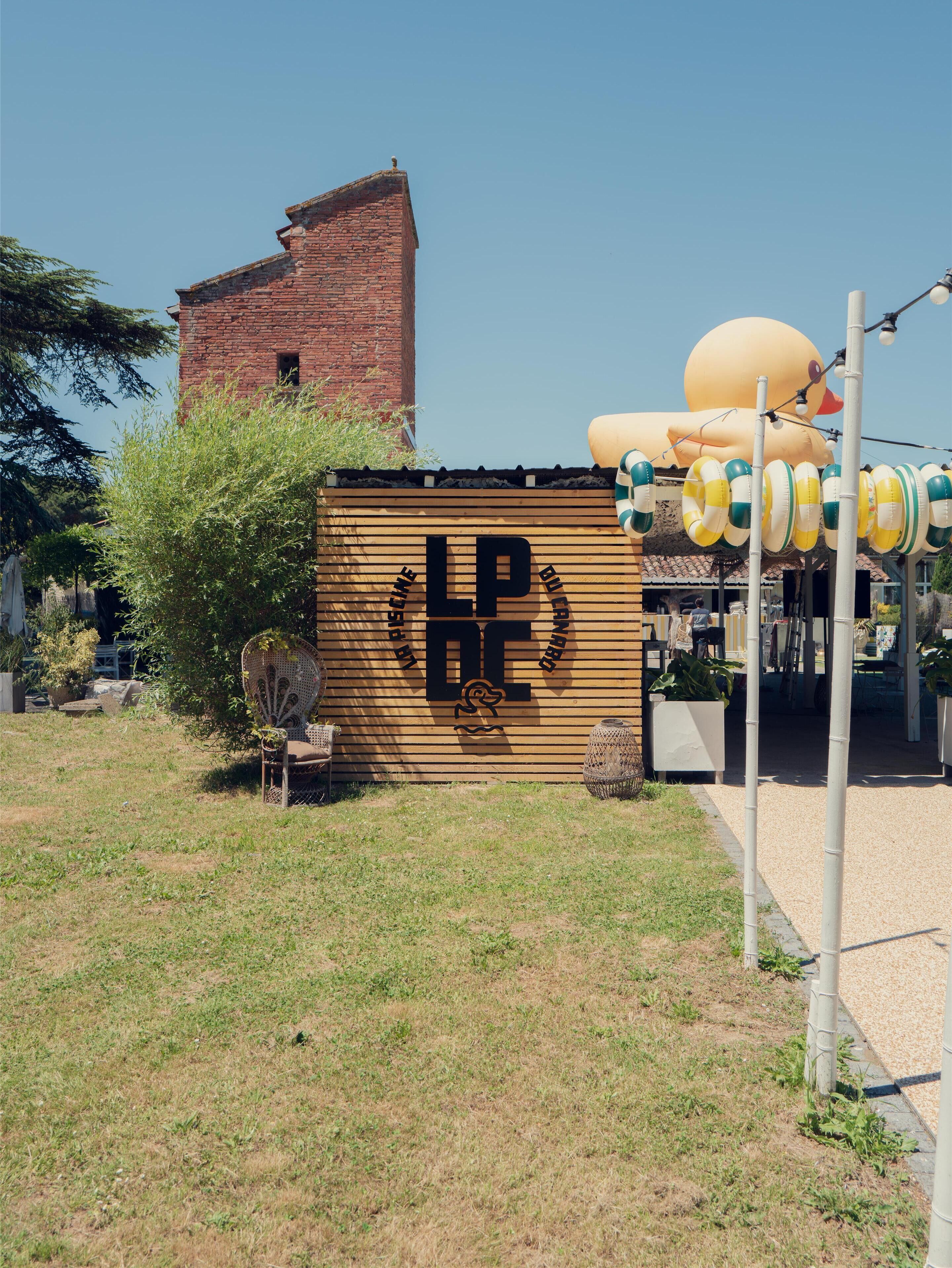 A wooden building with a large logo, a brick structure in the background, and a decorative inflatable duck.