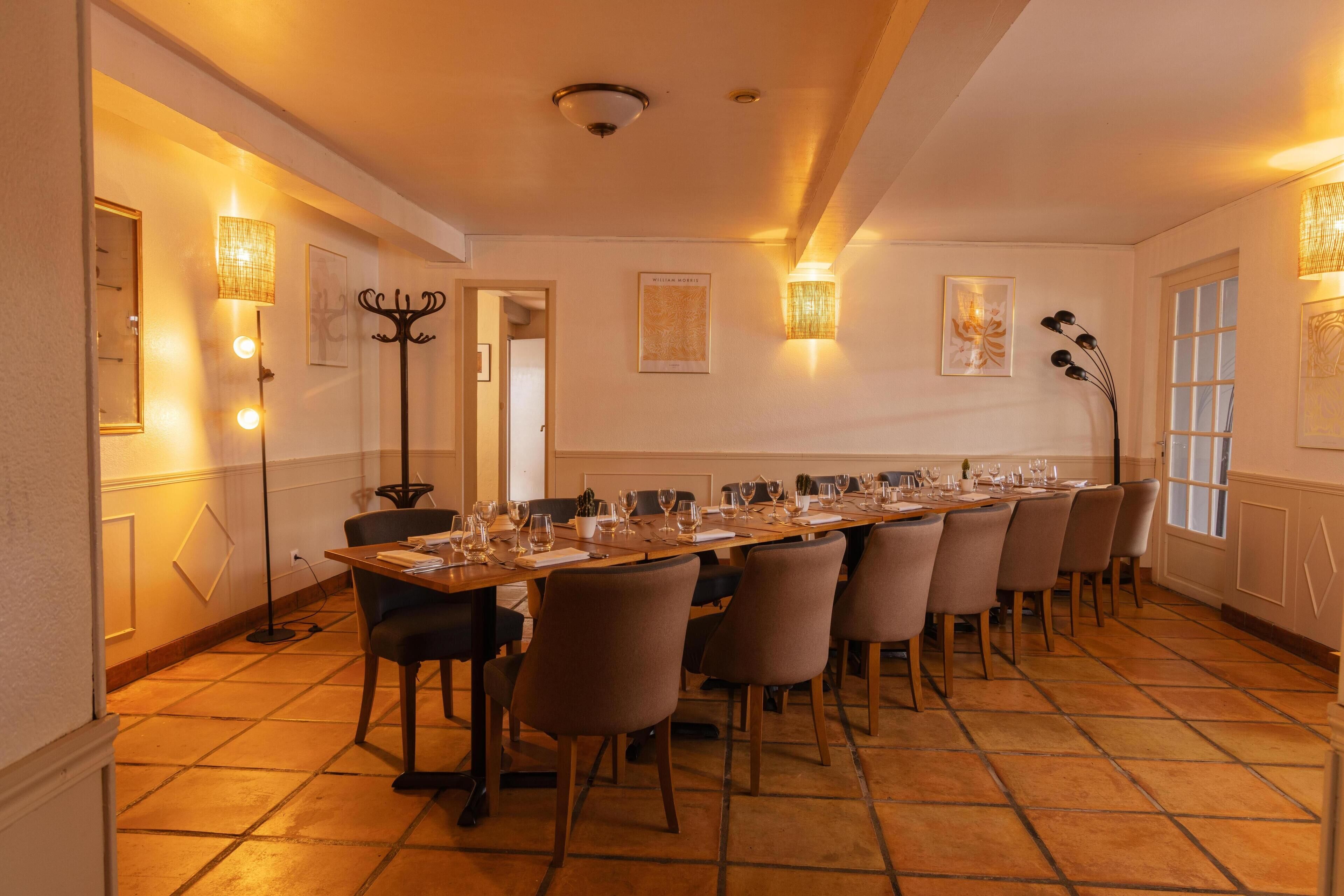 A long dining table set for a meal, flanked by chairs, in a room with tiled flooring and wall-mounted lighting fixtures.