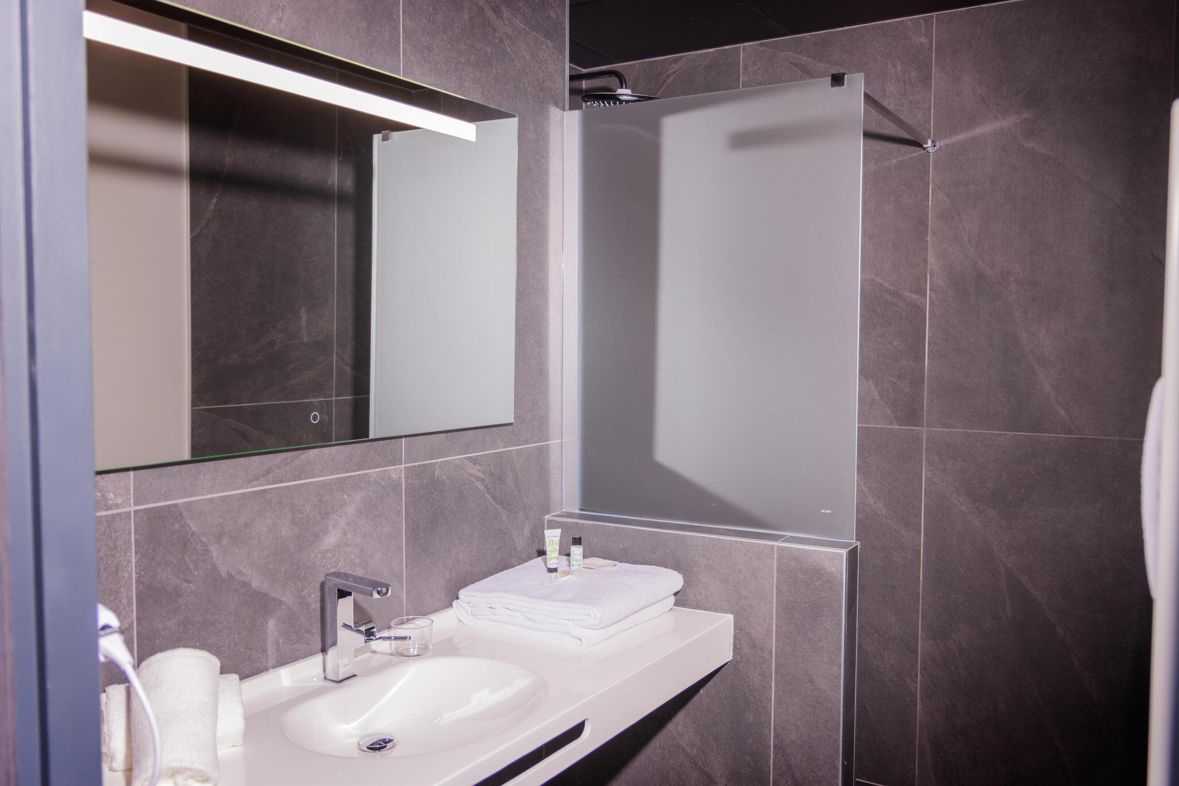 Un baño moderno con un lavamanos blanco, un espejo y una zona de ducha.