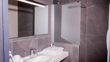 Un baño moderno con un lavamanos blanco, un espejo y una zona de ducha.