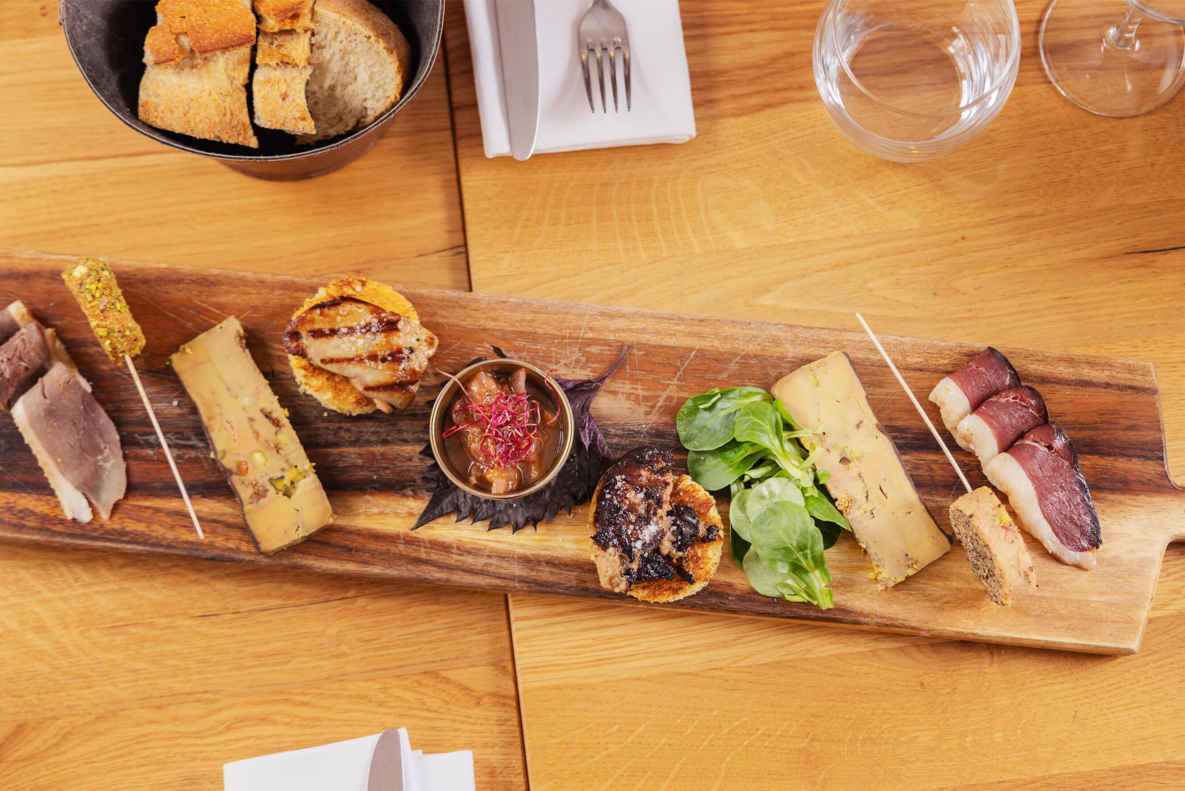 A wooden board with various food items including meats, cheeses, and vegetables.