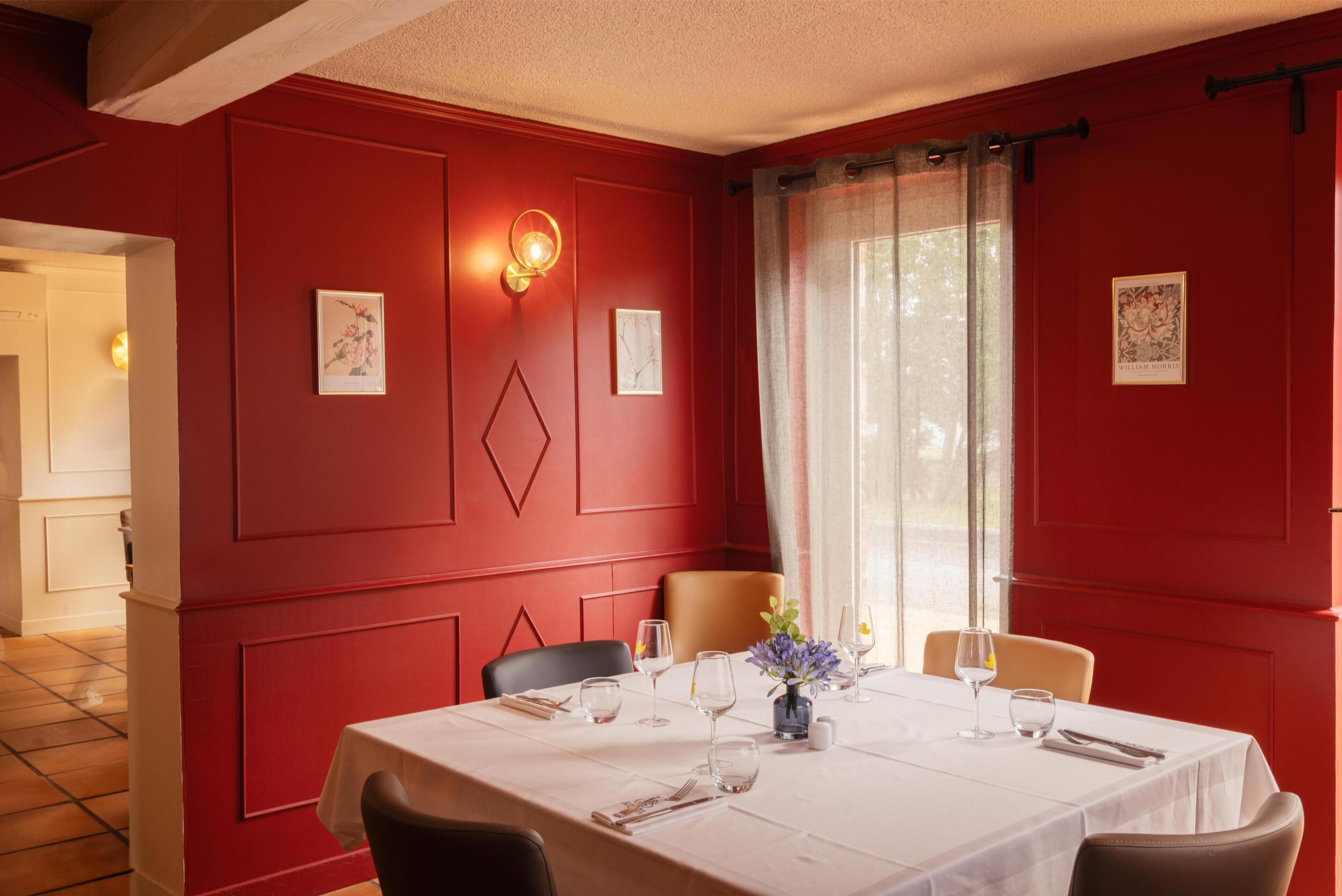 A dining area with a red wall, a white table, and a vase of flowers.