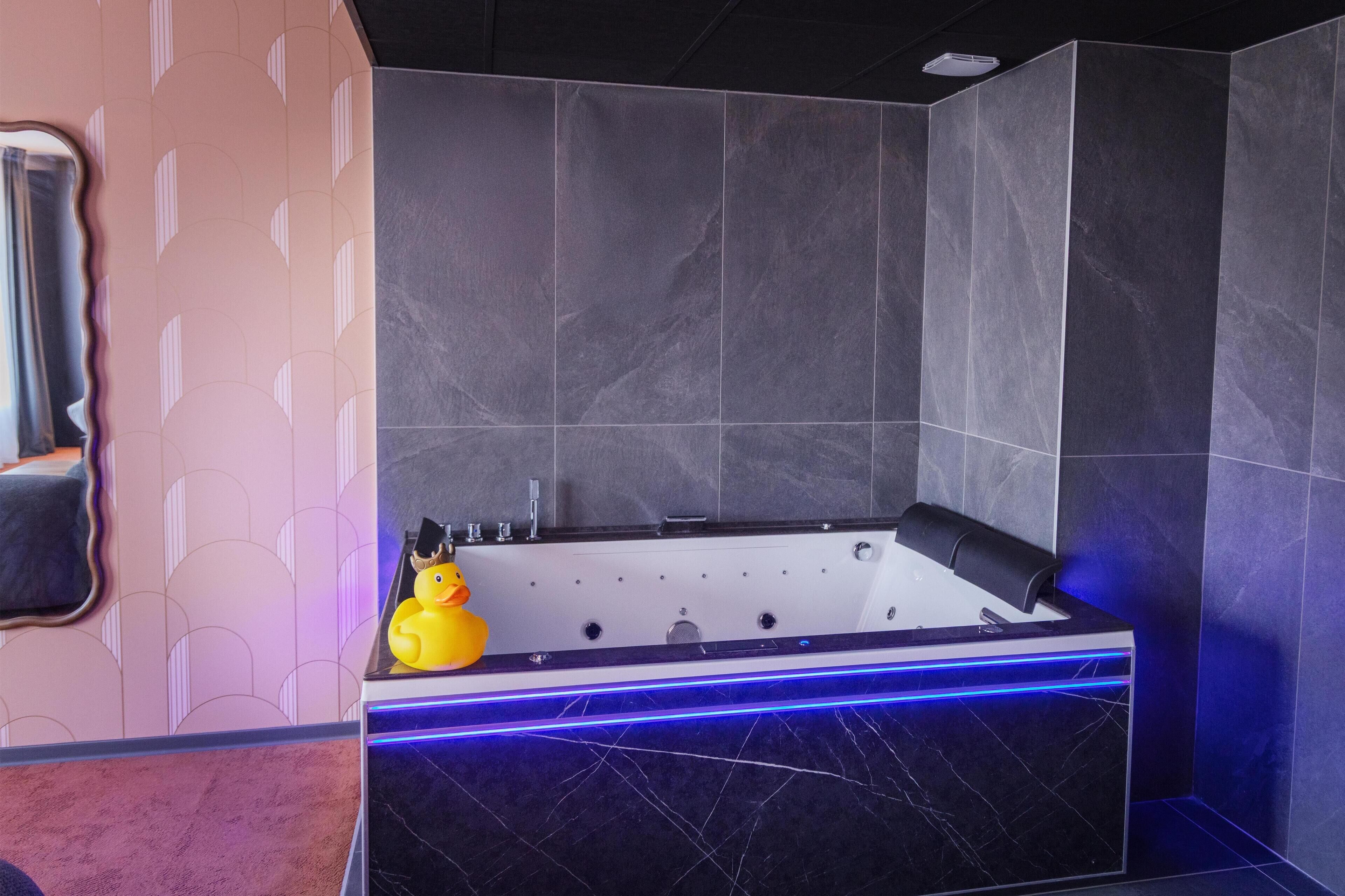 A modern bathroom with a large bathtub, a yellow rubber duck, and a towel rack.