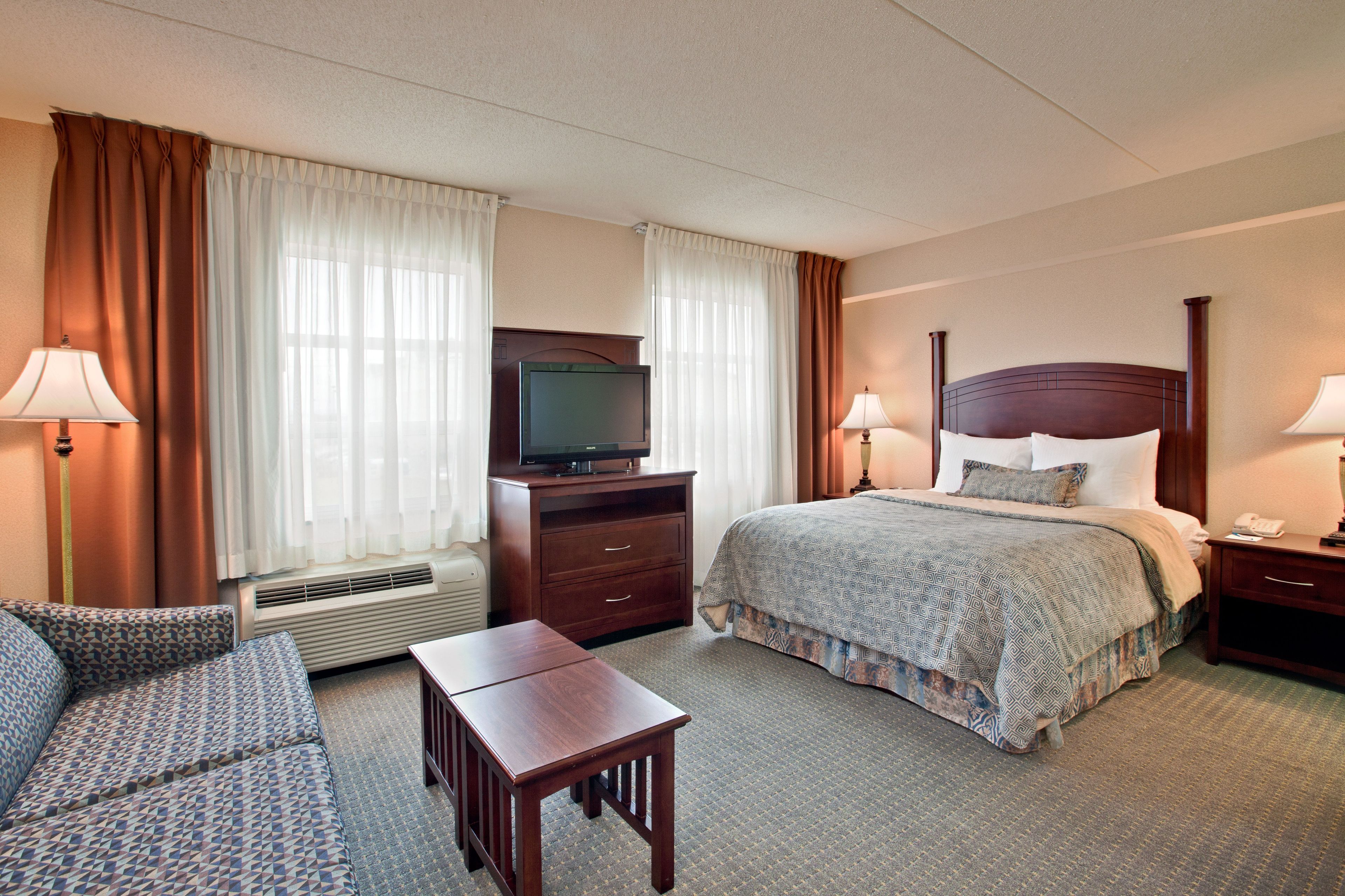 Een hotelkamer met een bed, een televisie, een bureau, een stoel en een bank.