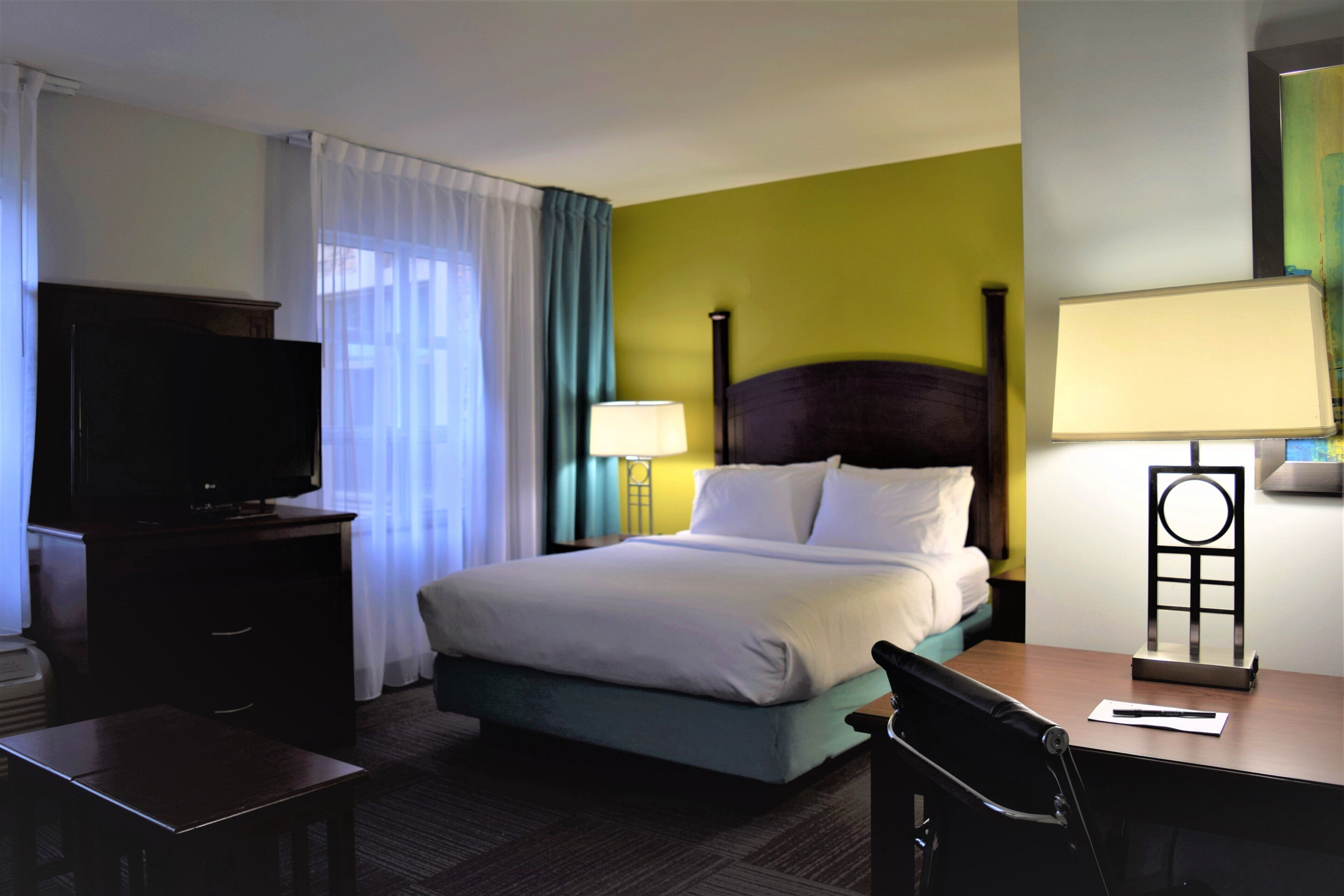 A hotel room with a bed, a desk, a television, and a lamp.