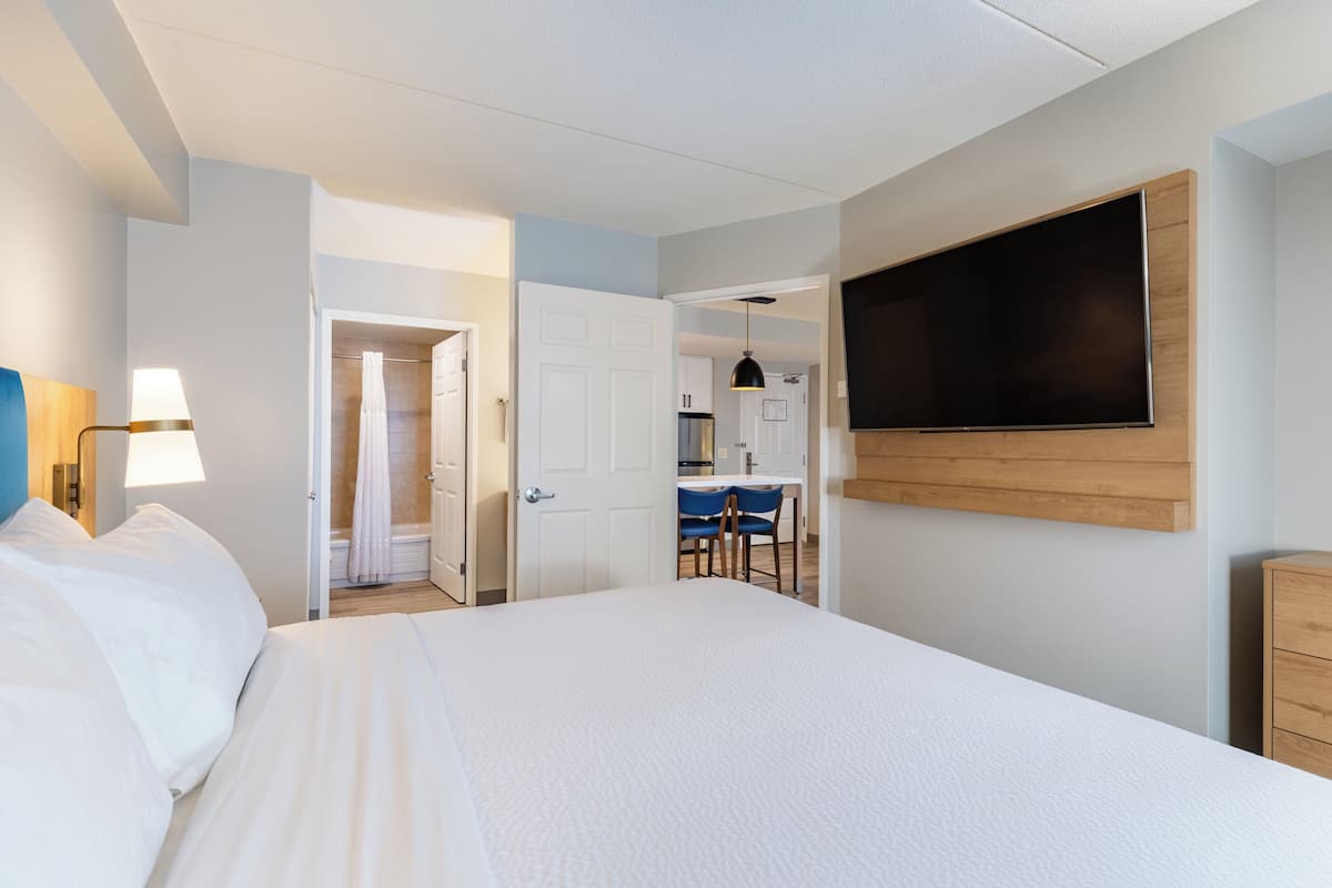 A hotel room with a large bed, a TV mounted on the wall, a desk with a chair, and a shower area.