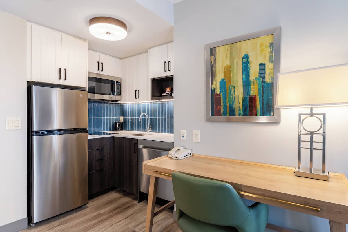 A modern kitchen with stainless steel appliances, a wooden dining table, and a cityscape painting on the wall.