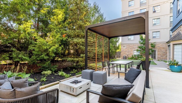 Un patio exterior con una zona de estar techada, una chimenea y vistas a un edificio al fondo.