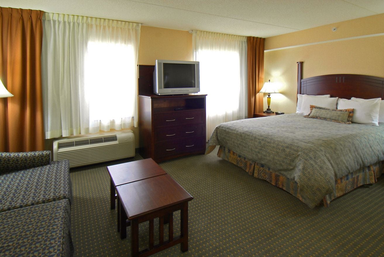 Ein Hotelzimmer mit einem Bett, einem Fernseher auf einer Kommode, einem Schreibtisch und einem Sofa.