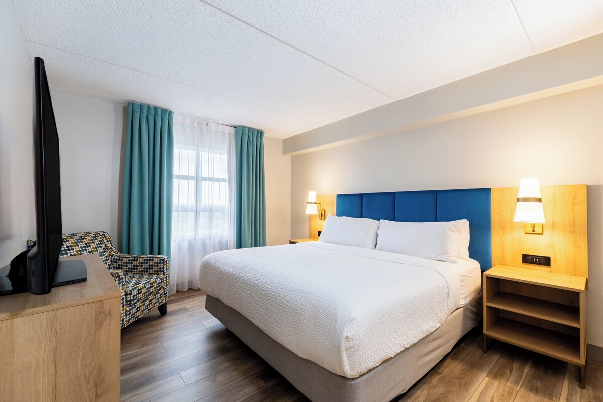 Een hotelkamer met een groot bed, twee bedlampen, een houten nachtkastje, een televisie op een bureau en een fauteuil met een patroon.